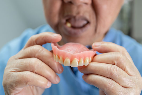 Person holding removable denture, known as false teeth showing that the denture can be removed